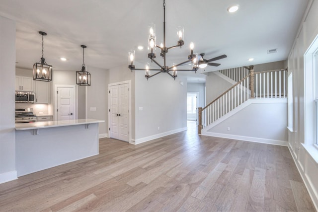 kitchen with appliances with stainless steel finishes, decorative light fixtures, white cabinetry, a breakfast bar area, and light hardwood / wood-style floors