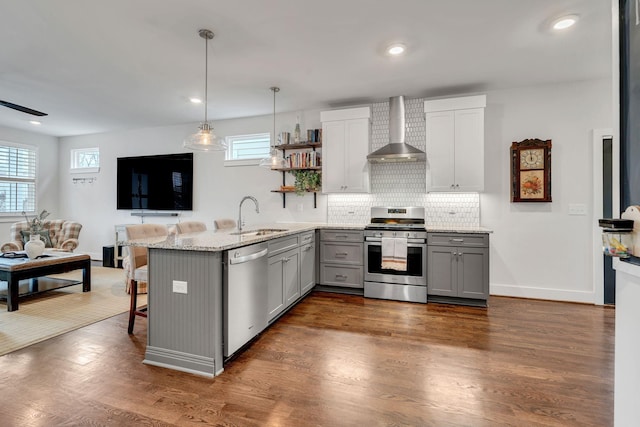 kitchen featuring a breakfast bar, sink, gray cabinetry, stainless steel appliances, and wall chimney range hood