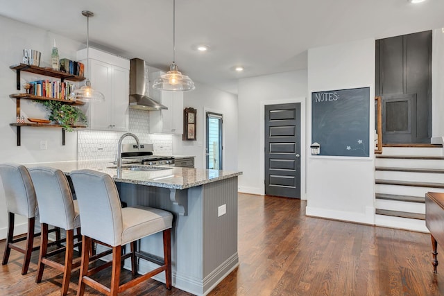 kitchen with wall chimney range hood, hanging light fixtures, stainless steel range oven, a kitchen bar, and kitchen peninsula