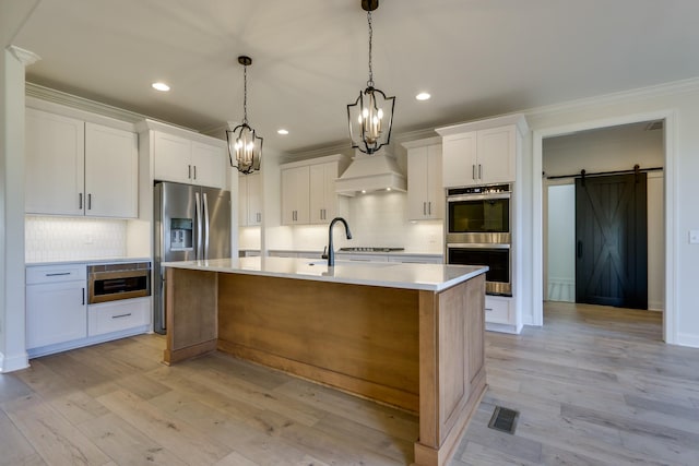 kitchen with pendant lighting, stainless steel appliances, a barn door, a kitchen island with sink, and white cabinets