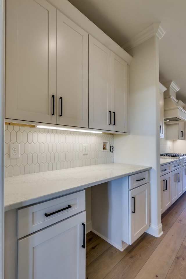 kitchen featuring backsplash, light stone countertops, light wood-type flooring, and white cabinets