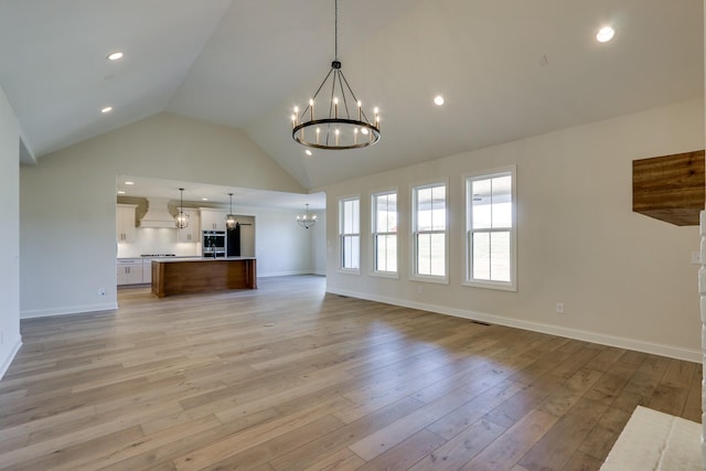 unfurnished living room featuring an inviting chandelier, high vaulted ceiling, and light wood-type flooring