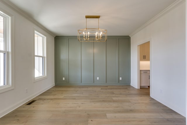 unfurnished dining area featuring a notable chandelier, crown molding, and light hardwood / wood-style floors