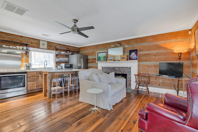 living room featuring dark hardwood / wood-style flooring, a brick fireplace, ceiling fan, and wood walls