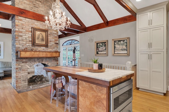 kitchen featuring vaulted ceiling with beams, decorative light fixtures, light wood-type flooring, stainless steel microwave, and a fireplace