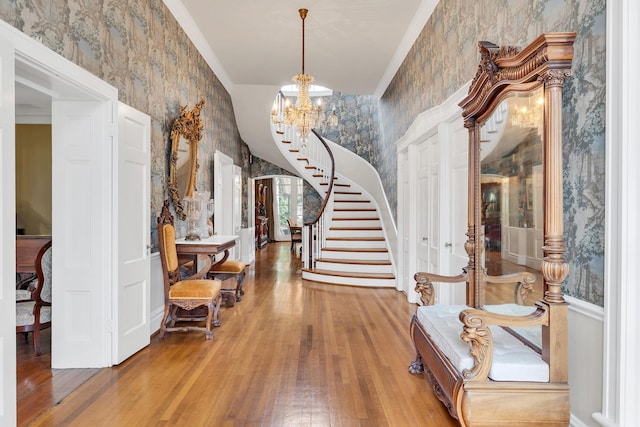 foyer entrance featuring hardwood / wood-style flooring, ornamental molding, and a notable chandelier