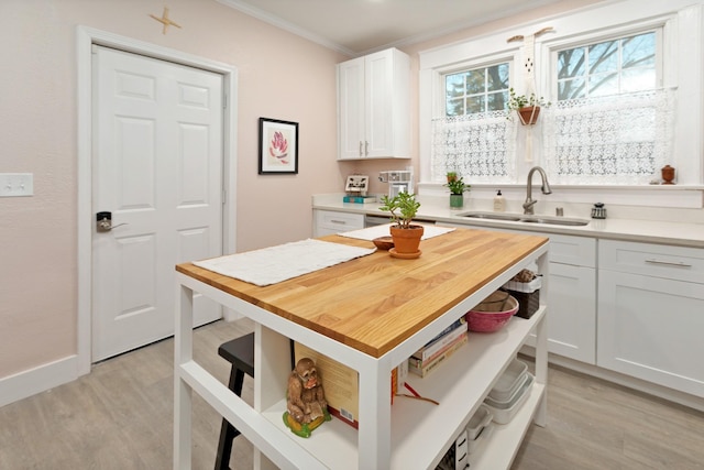 kitchen featuring butcher block counters, sink, white cabinetry, ornamental molding, and light hardwood / wood-style floors