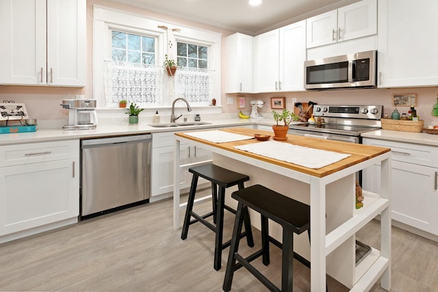 kitchen with sink, a breakfast bar, appliances with stainless steel finishes, light hardwood / wood-style floors, and white cabinets