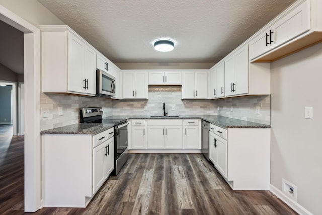 kitchen featuring dark hardwood / wood-style floors, sink, white cabinets, dark stone counters, and stainless steel appliances