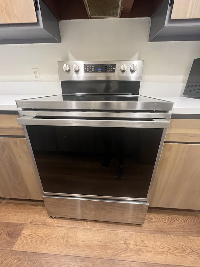 interior space featuring stainless steel electric range, light wood-type flooring, ventilation hood, and light brown cabinets