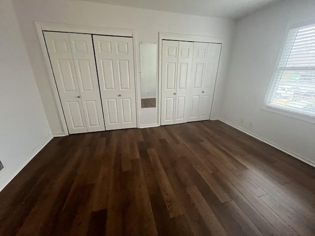 unfurnished bedroom with dark wood-type flooring and multiple closets