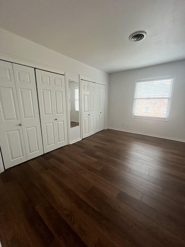 unfurnished bedroom featuring dark hardwood / wood-style flooring and two closets