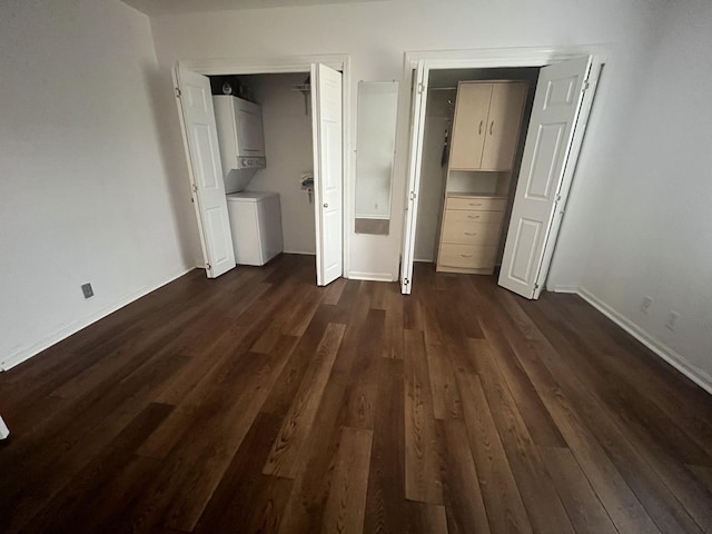 unfurnished bedroom featuring dark wood-type flooring, stacked washing maching and dryer, and two closets