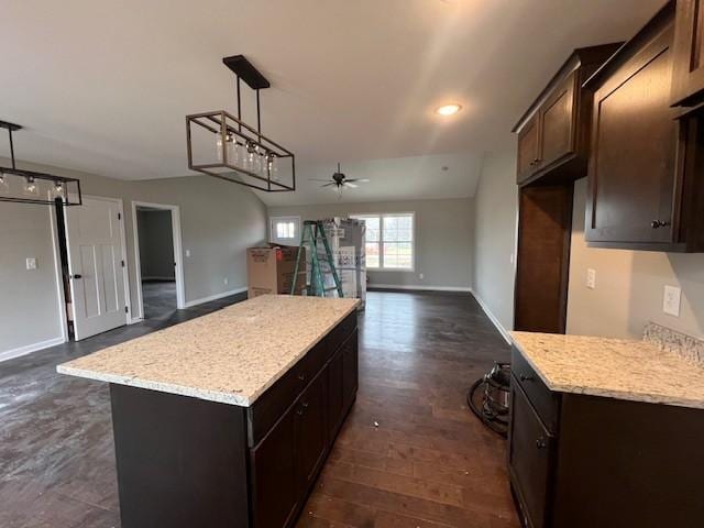 kitchen with a center island, hanging light fixtures, dark brown cabinets, ceiling fan, and light stone countertops