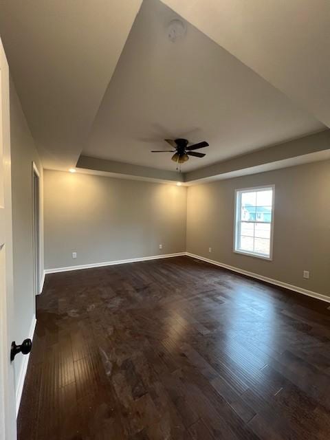 spare room featuring dark hardwood / wood-style floors, ceiling fan, and a tray ceiling