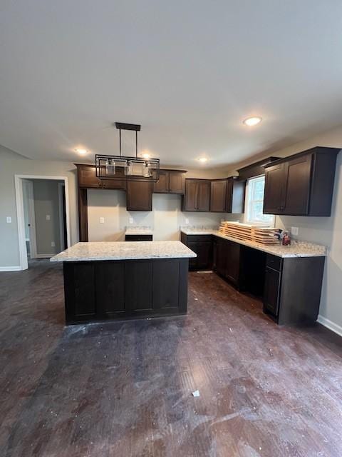 kitchen featuring pendant lighting, dark brown cabinets, light stone countertops, and a center island