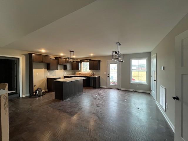 kitchen with pendant lighting, dark brown cabinetry, a kitchen island, and a notable chandelier