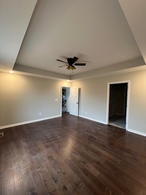 empty room with dark wood-type flooring, a raised ceiling, and ceiling fan