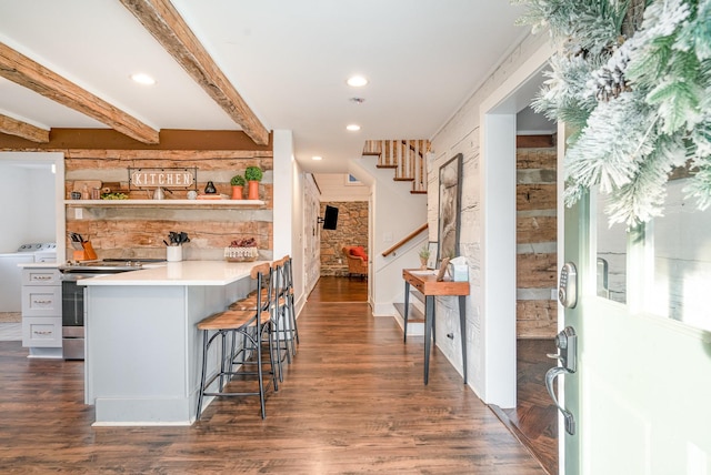 kitchen with stainless steel electric stove, washing machine and dryer, dark hardwood / wood-style floors, and a kitchen bar