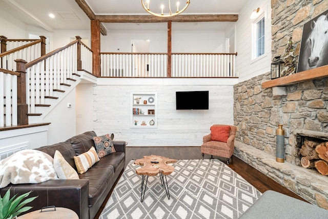 living room with a stone fireplace, beamed ceiling, hardwood / wood-style flooring, a high ceiling, and an inviting chandelier