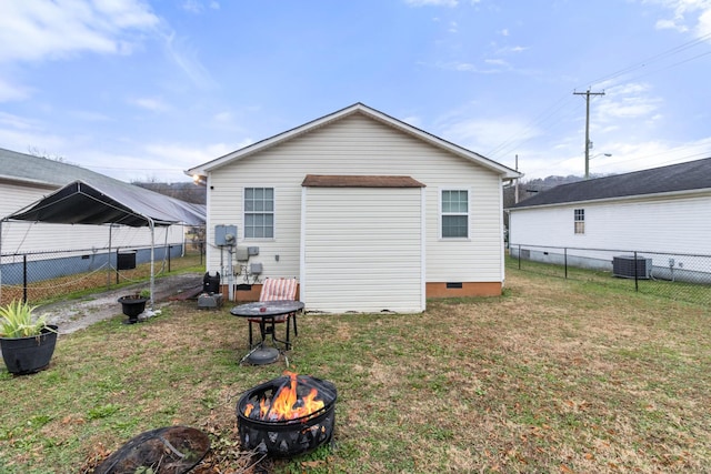 rear view of property featuring crawl space, central AC, a fire pit, and a lawn