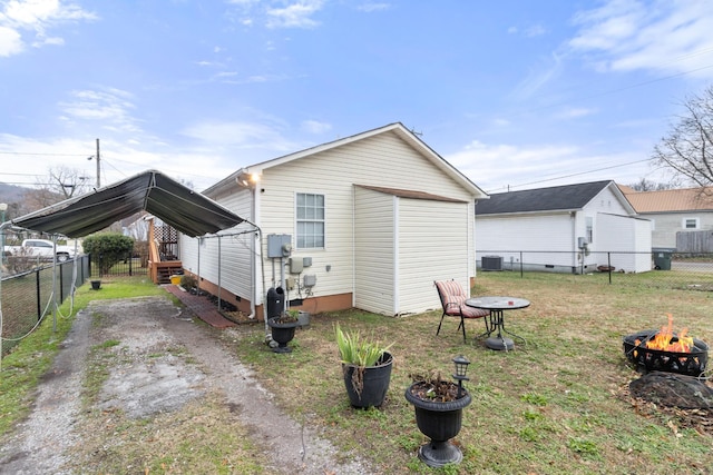 rear view of house with an outdoor fire pit, fence, dirt driveway, a lawn, and a carport