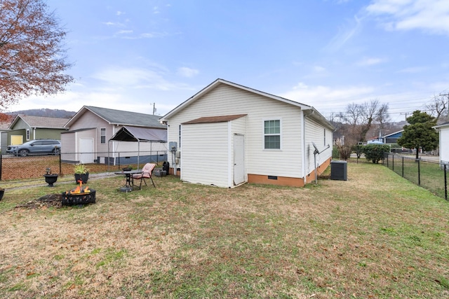 back of property with a fire pit, a lawn, crawl space, fence, and central air condition unit