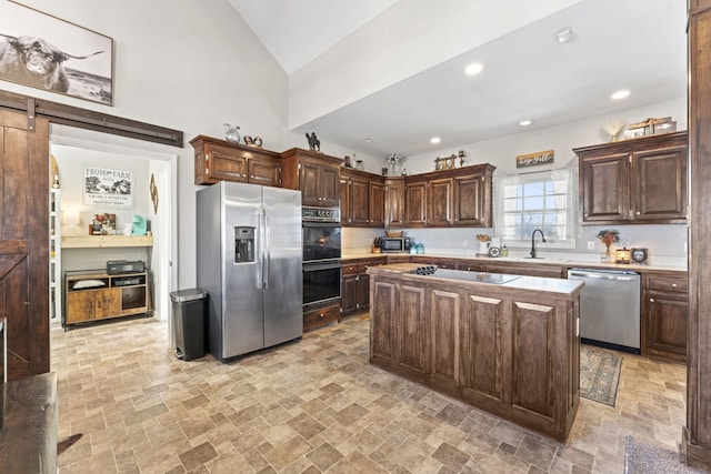 kitchen with dark brown cabinetry, sink, a center island, a barn door, and black appliances