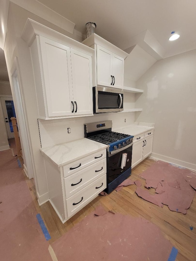 kitchen with appliances with stainless steel finishes, lofted ceiling, white cabinets, light stone countertops, and light hardwood / wood-style flooring