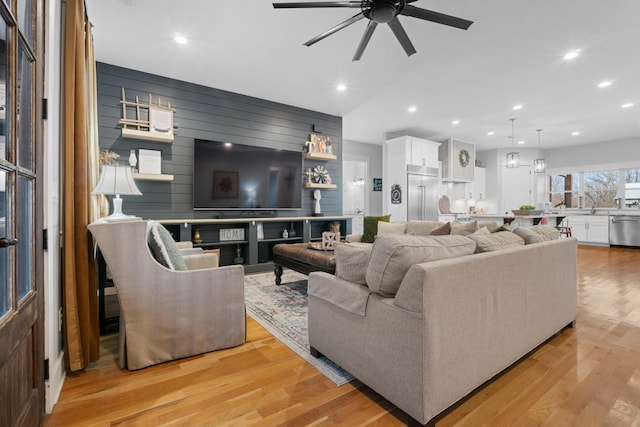 living room with ceiling fan, wooden walls, and light wood-type flooring