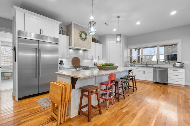 kitchen featuring appliances with stainless steel finishes, white cabinetry, a center island, light stone countertops, and decorative light fixtures