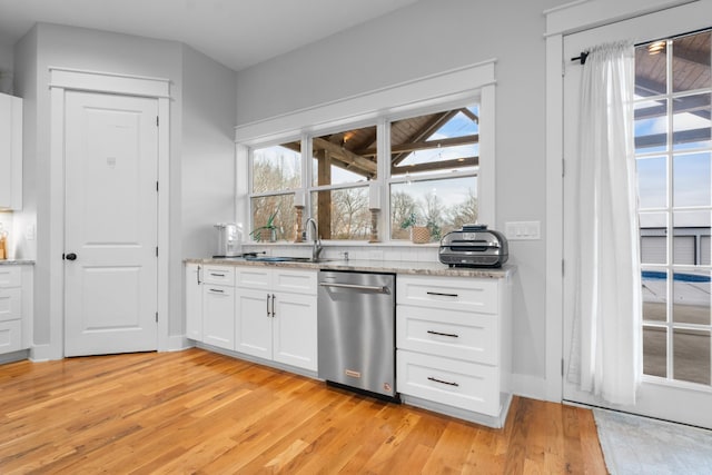 kitchen with sink, white cabinetry, light wood-type flooring, stainless steel dishwasher, and light stone countertops