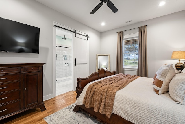 bedroom featuring ceiling fan, a barn door, light wood-type flooring, and ensuite bath