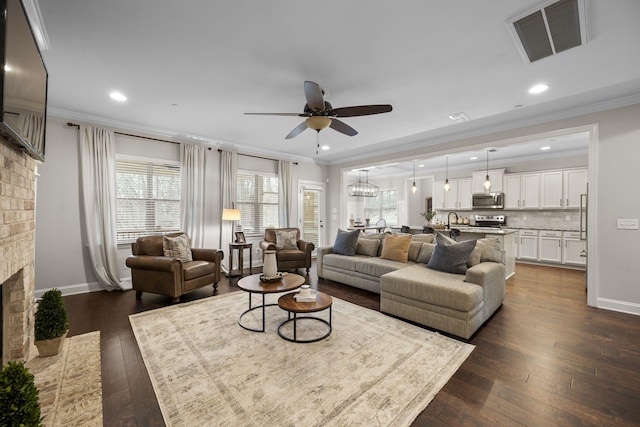 living room with dark hardwood / wood-style flooring, crown molding, a fireplace, and ceiling fan with notable chandelier