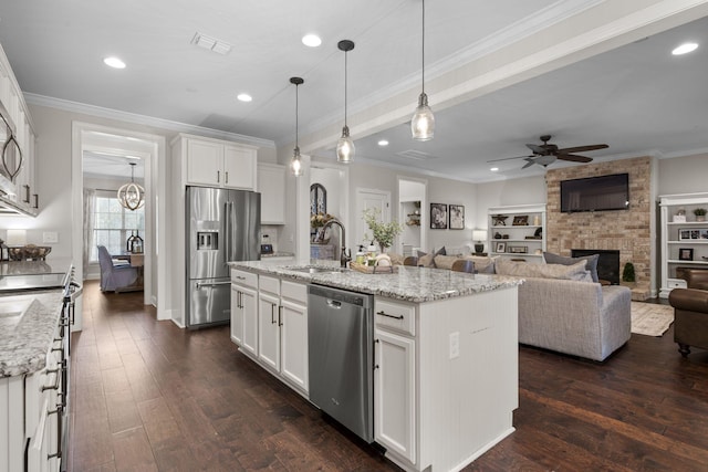 kitchen with stainless steel appliances, a kitchen island with sink, white cabinets, and light stone counters