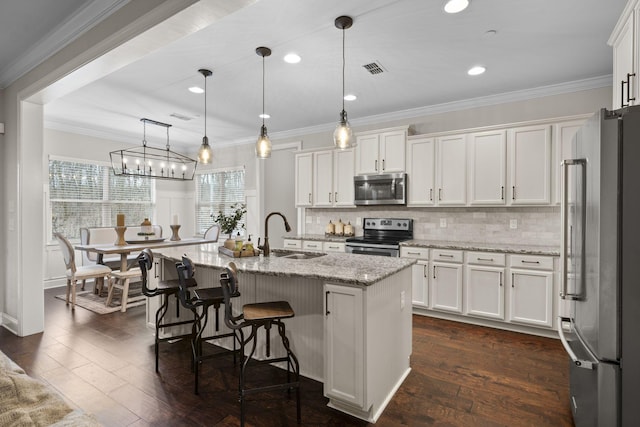 kitchen featuring appliances with stainless steel finishes, white cabinetry, sink, hanging light fixtures, and a kitchen island with sink