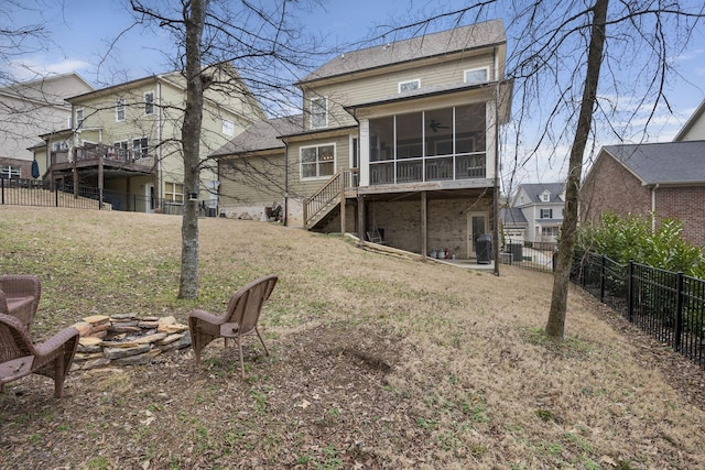 rear view of house with a sunroom, a yard, and an outdoor fire pit