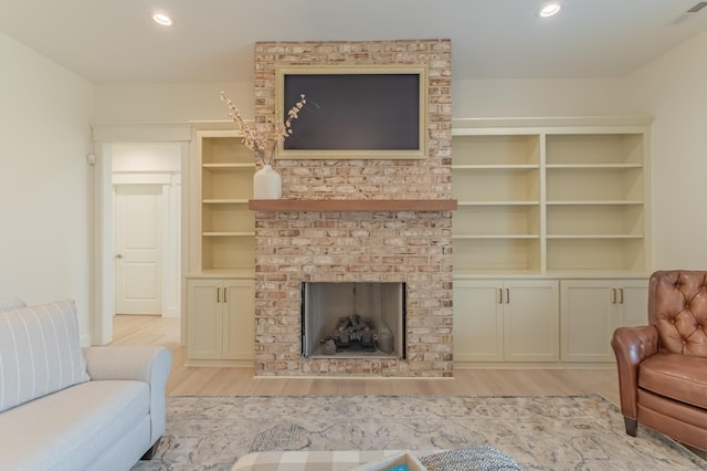 living room featuring built in shelves, a fireplace, and light wood-type flooring