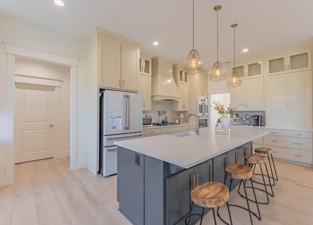 kitchen with sink, decorative light fixtures, appliances with stainless steel finishes, custom range hood, and a kitchen island with sink