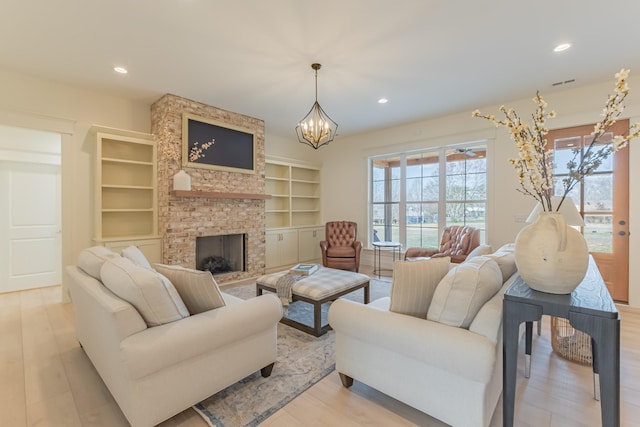 living room with light hardwood / wood-style flooring, built in shelves, a fireplace, and a chandelier