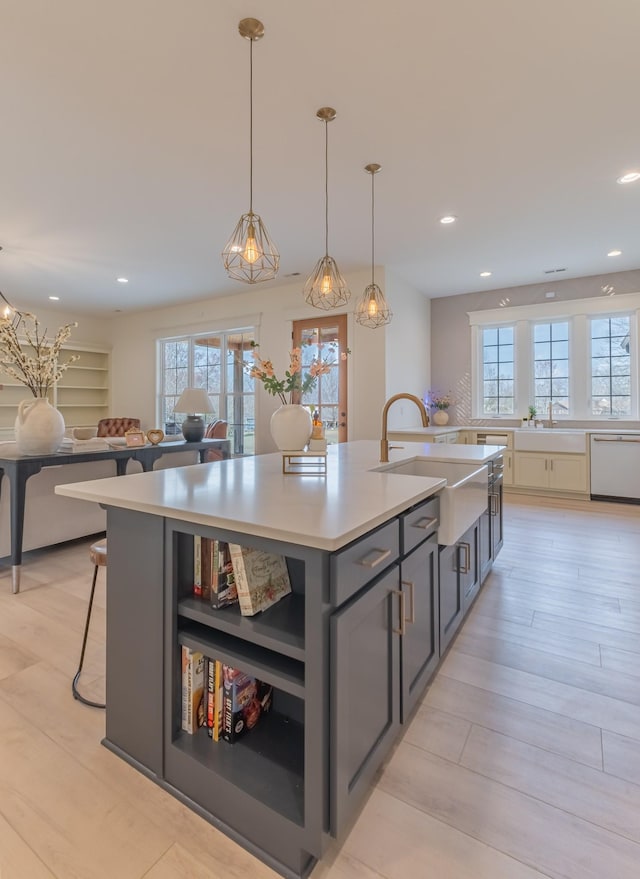 kitchen with sink, hanging light fixtures, white dishwasher, a center island with sink, and light hardwood / wood-style flooring