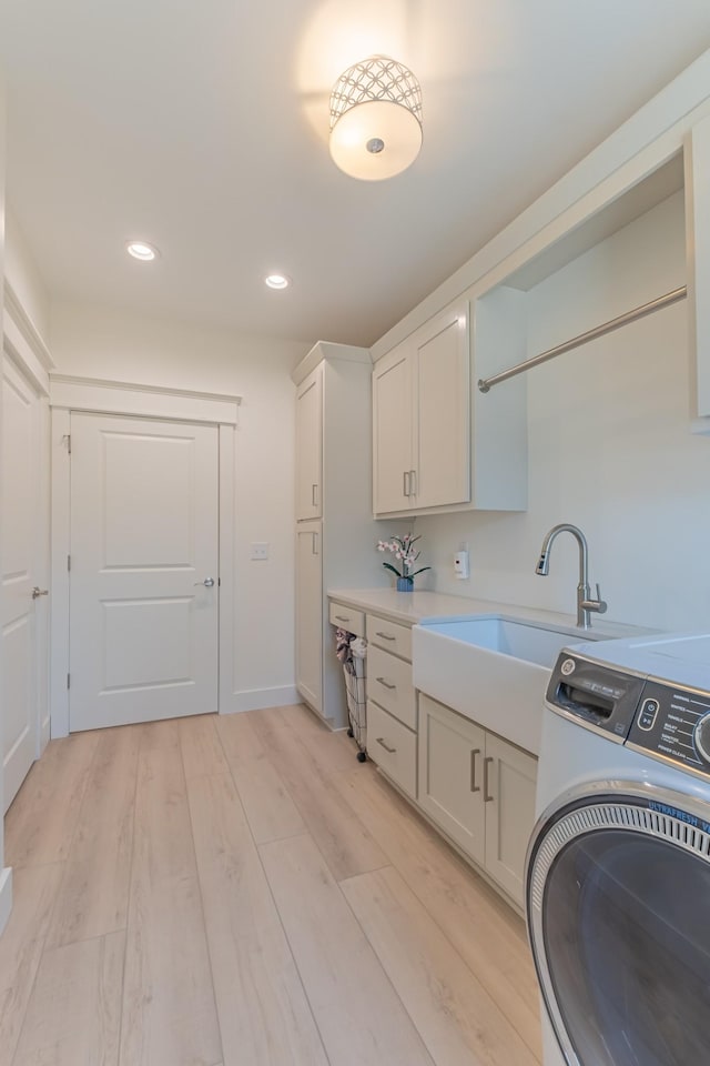 laundry area featuring cabinets, washer / clothes dryer, sink, and light hardwood / wood-style flooring