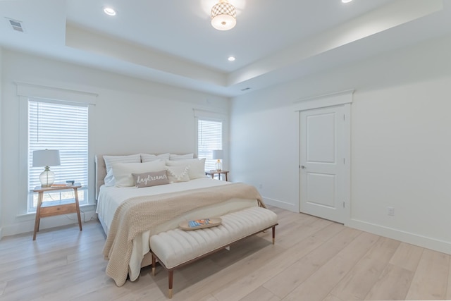 bedroom with a tray ceiling and light hardwood / wood-style floors