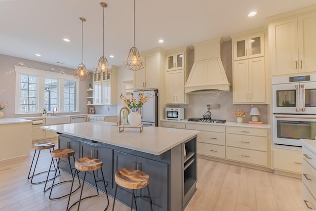 kitchen with a kitchen bar, custom exhaust hood, hanging light fixtures, an island with sink, and white appliances