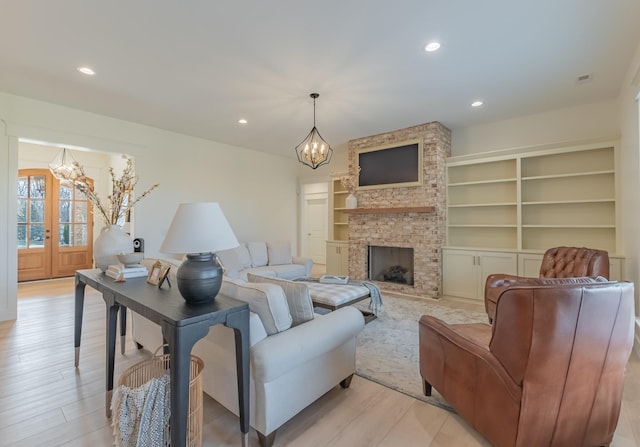 living room featuring an inviting chandelier, a stone fireplace, french doors, and light wood-type flooring