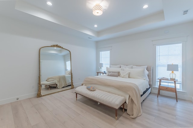 bedroom featuring a raised ceiling and light wood-type flooring