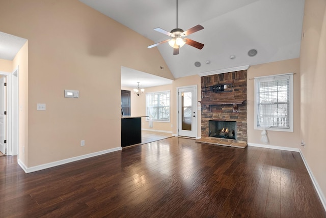 unfurnished living room featuring dark hardwood / wood-style flooring, a stone fireplace, ceiling fan with notable chandelier, and high vaulted ceiling