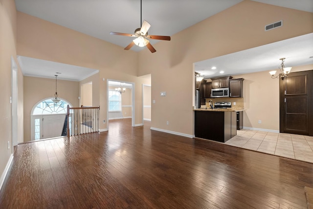 unfurnished living room with high vaulted ceiling, sink, ceiling fan with notable chandelier, and light hardwood / wood-style floors