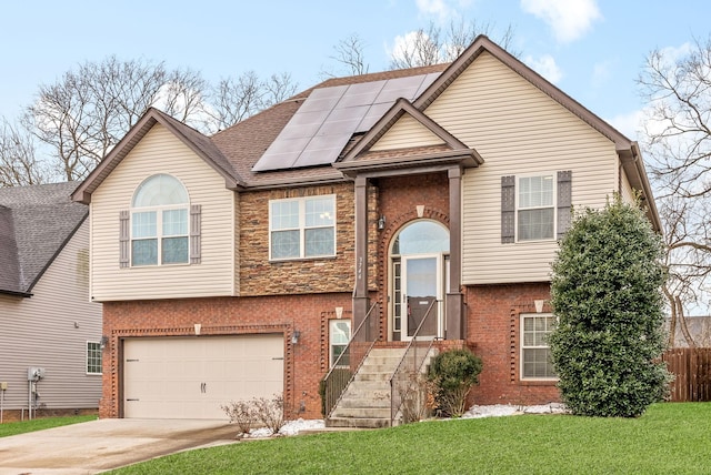 raised ranch featuring a garage, a front yard, and solar panels