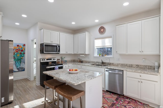 kitchen featuring a breakfast bar area, light stone counters, a center island, appliances with stainless steel finishes, and white cabinets